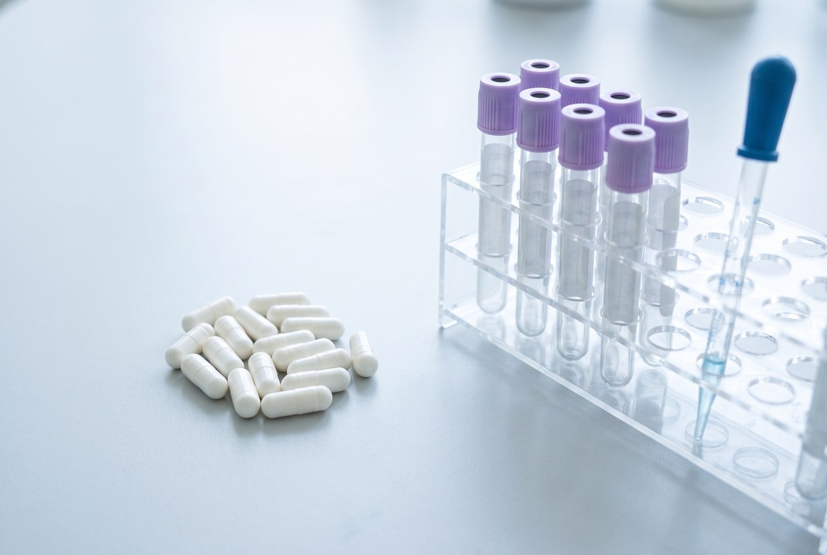 Plain white capsules on a pale grey bench beside a rack of clear blood collection tubes with lavender caps and a pipette, photographed for Magellan Longevity's review of what NAD and NMN trials actually measured.
